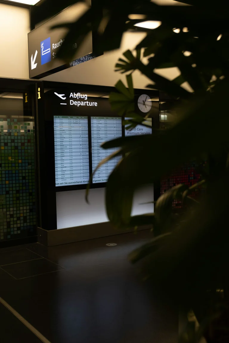 Departure screen at Vienna Airport with clock and signage, partially hidden by indoor plants